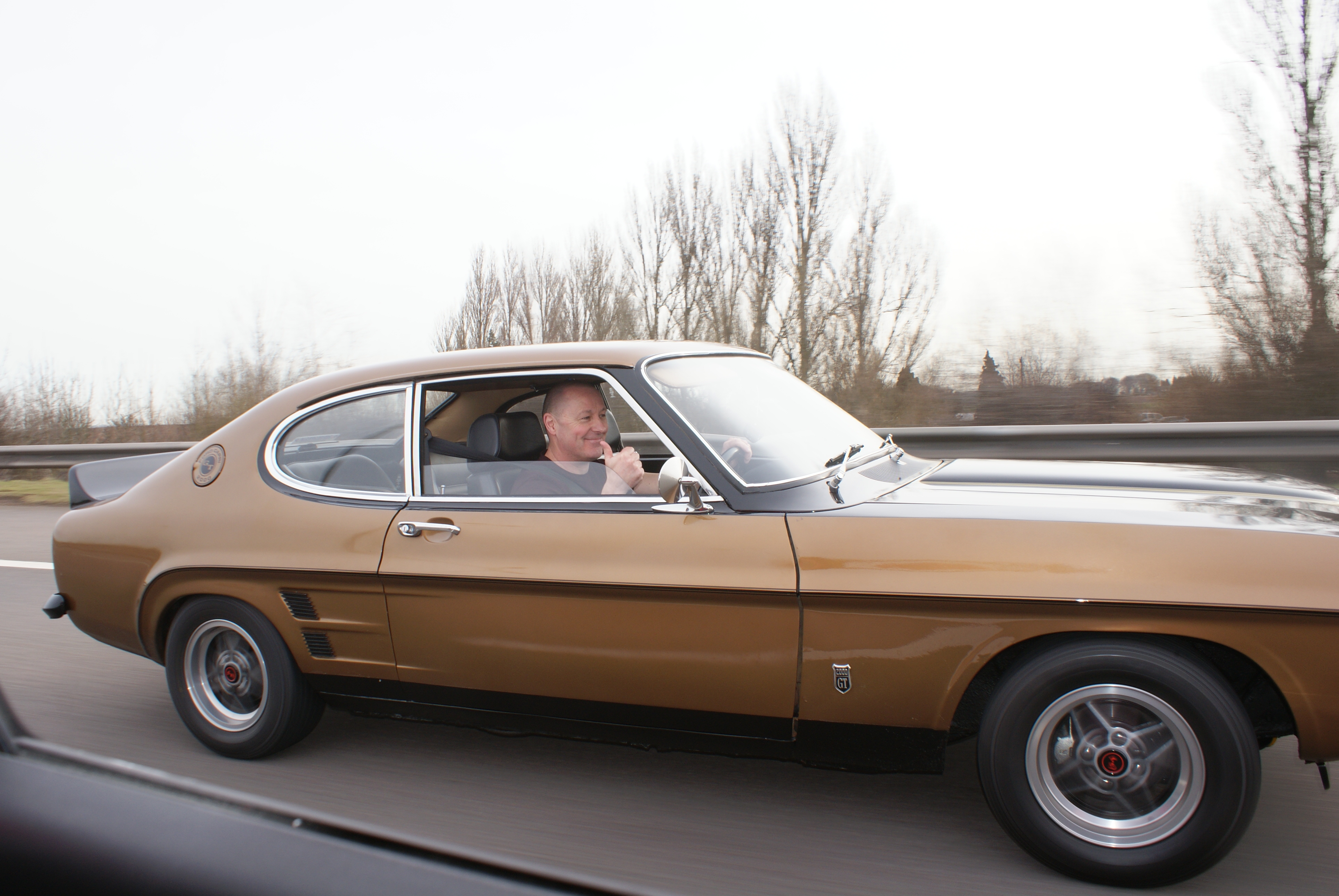 Gold and black custom mk1 ford capri, driving along the m6 motorway at speed on route to the NEC